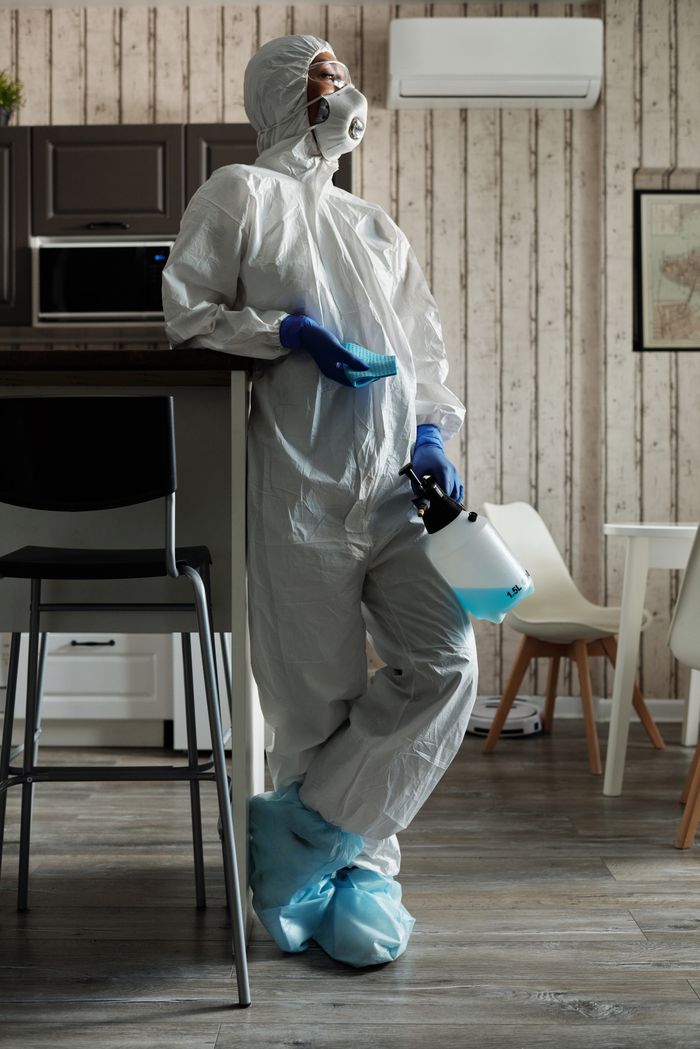 Individual wearing full protective gear indoors with disinfectant spray equipment.